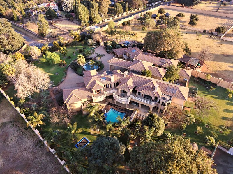 Aerial view of a large residential property featuring a swimming pool, extensive landscaped gardens, paved driveway, and multiple balconies under a tiled roof.