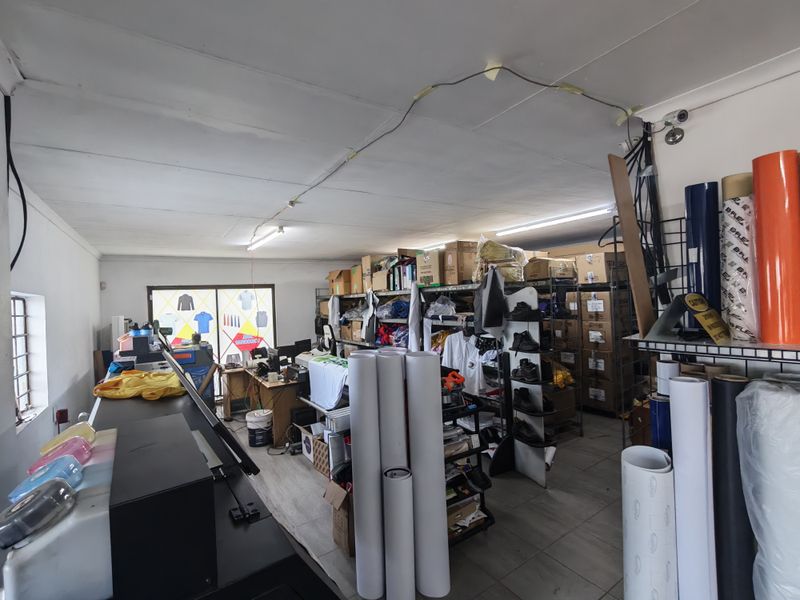 A functional utility or workspace area featuring tiled flooring, fluorescent lighting, and a sliding glass door, currently utilized for storage and production.