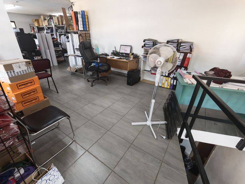 A functional office space featuring tiled flooring and access to a staircase, currently utilized for storage and administrative work.