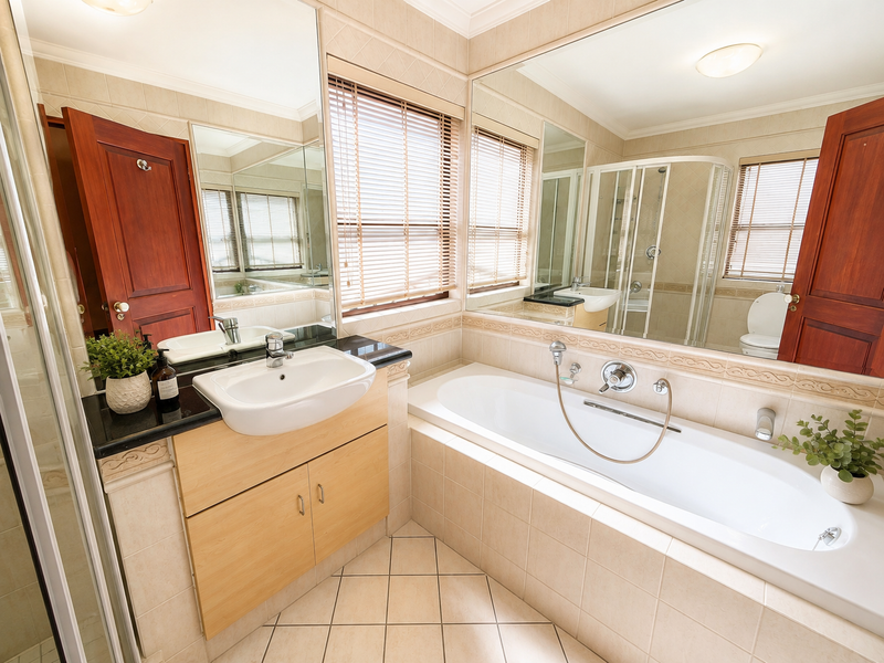 A well-maintained bathroom featuring a built-in vanity with a ceramic basin, a separate bathtub, a shower enclosure, and large wall mirrors.