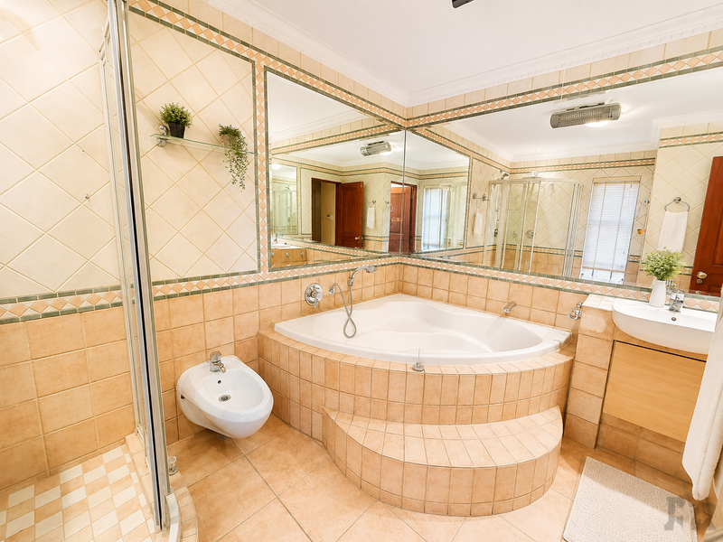 A spacious bathroom featuring a corner bathtub, bidet, glass-enclosed shower, and a large vanity mirror with classic tiled finishes.