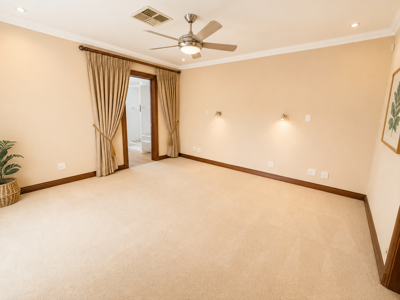 A spacious, well-maintained bedroom featuring neutral carpeting, recessed lighting, a ceiling fan, and wall-mounted accent lights, with a doorway leading to an adjacent room.