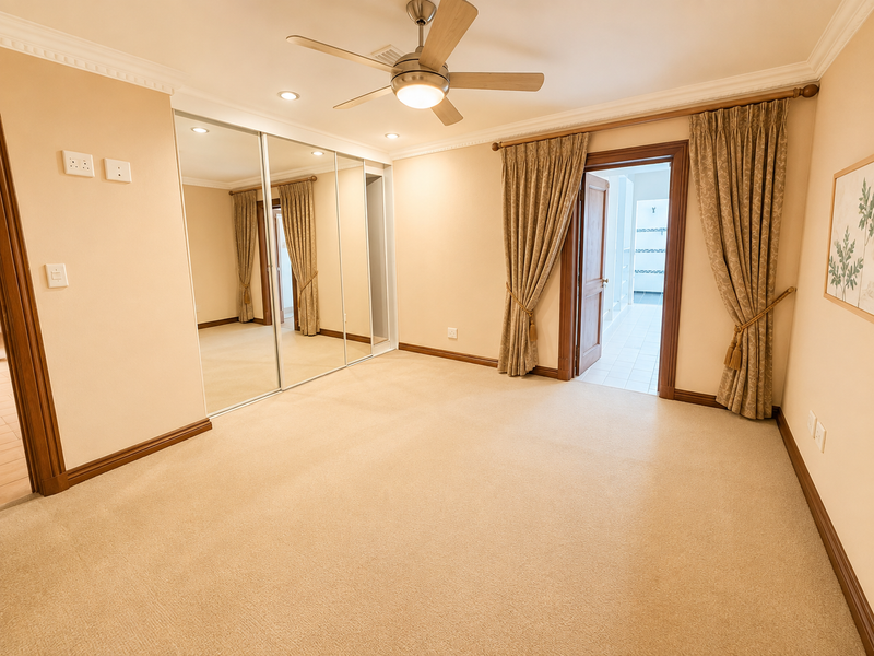 Spacious bedroom featuring neutral carpeting, mirrored built-in wardrobes, recessed lighting, and a ceiling fan, with direct access to an adjoining room.