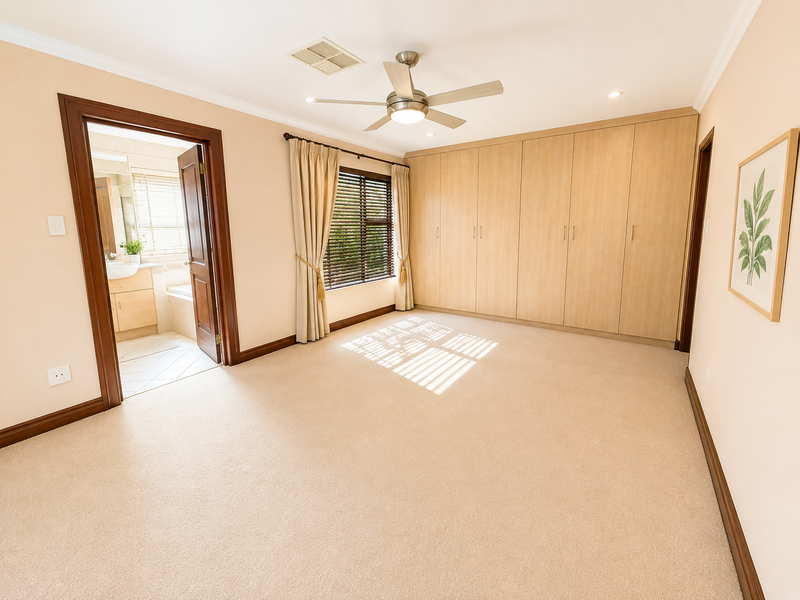 Spacious bedroom featuring neutral carpeting, extensive built-in cabinetry, a ceiling fan, and direct access to an en-suite bathroom.