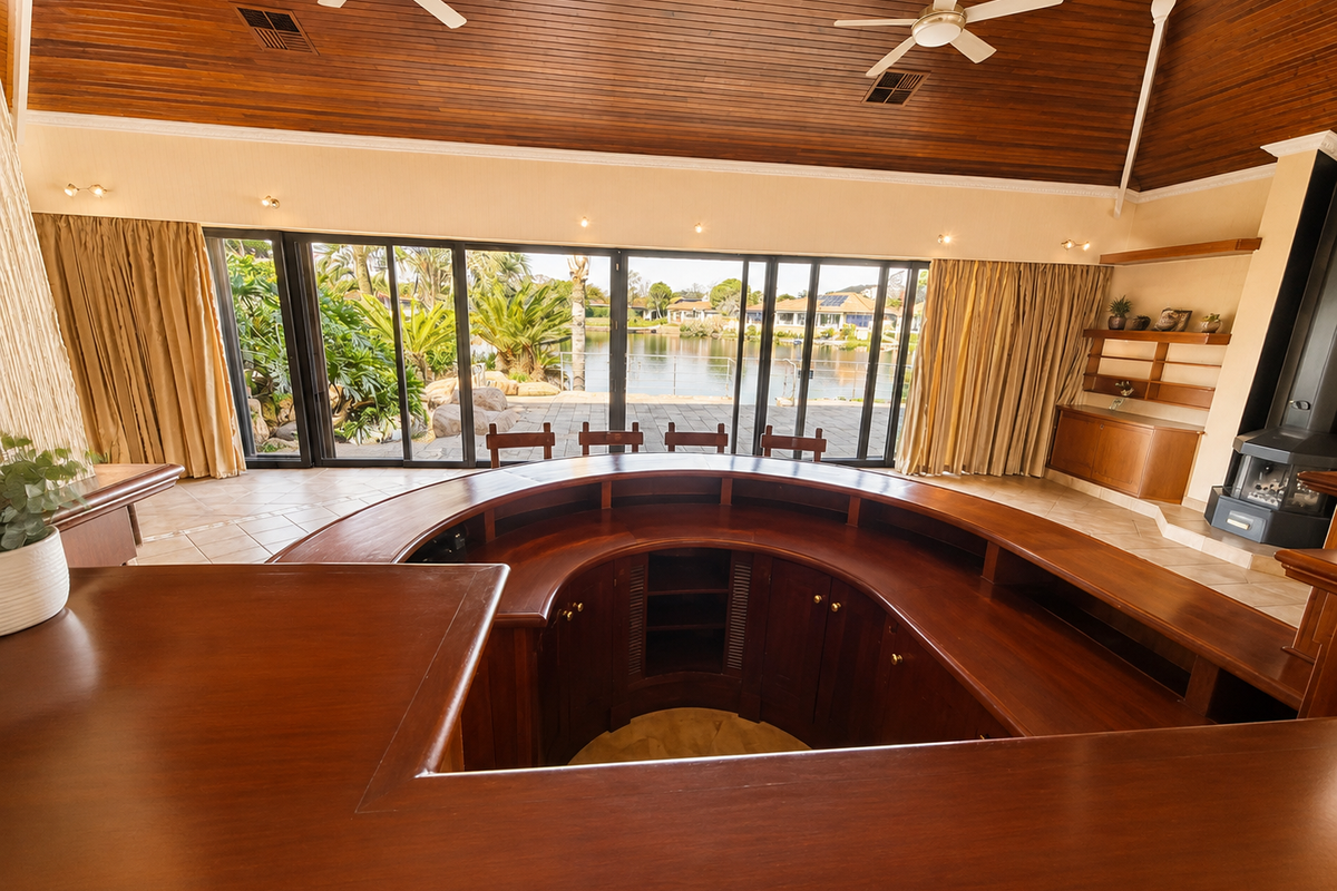 Spacious bar area featuring a large curved timber counter, vaulted timber ceiling, built-in fireplace, and expansive sliding doors opening to a waterfront view.