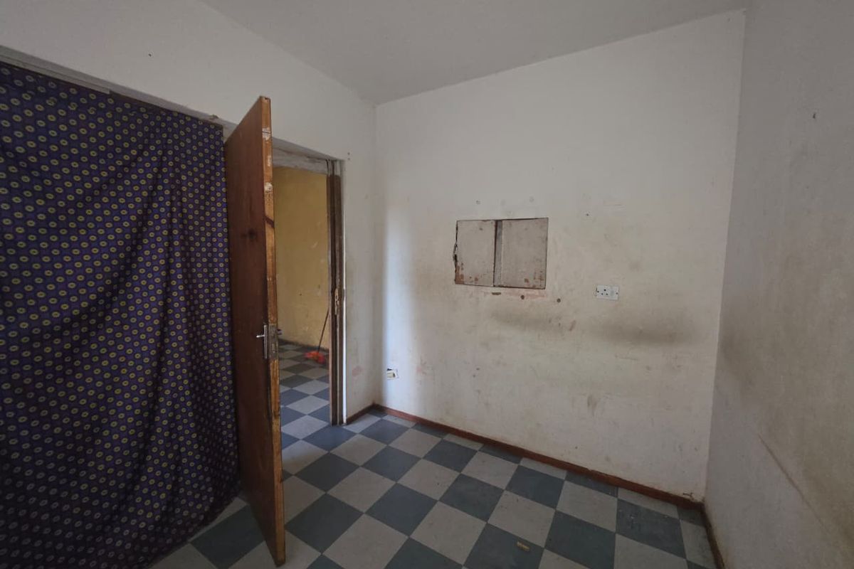 An empty bedroom featuring checkered floor tiles and a wooden door, requiring wall repairs and cosmetic updates to restore its condition.