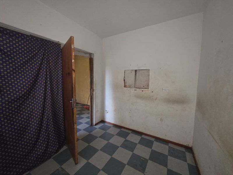 An empty bedroom featuring checkered floor tiles and a wooden door, requiring wall repairs and cosmetic updates to restore its condition.