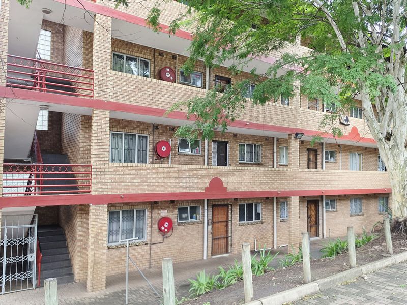 Exterior view of a multi-story apartment complex featuring face brick construction, external staircases, and security features on windows and doors.