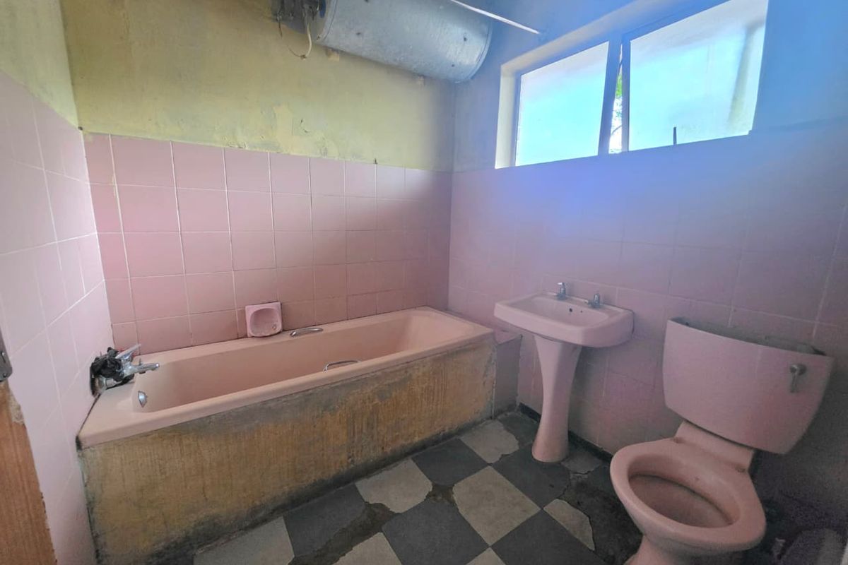 A dated bathroom featuring a pink suite, tiled walls, and floor, requiring significant renovation and modernization of fixtures and finishes.