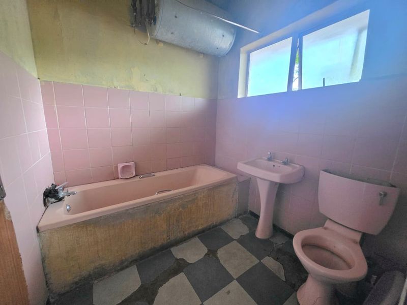 A dated bathroom featuring a pink suite, tiled walls, and floor, requiring significant renovation and modernization of fixtures and finishes.