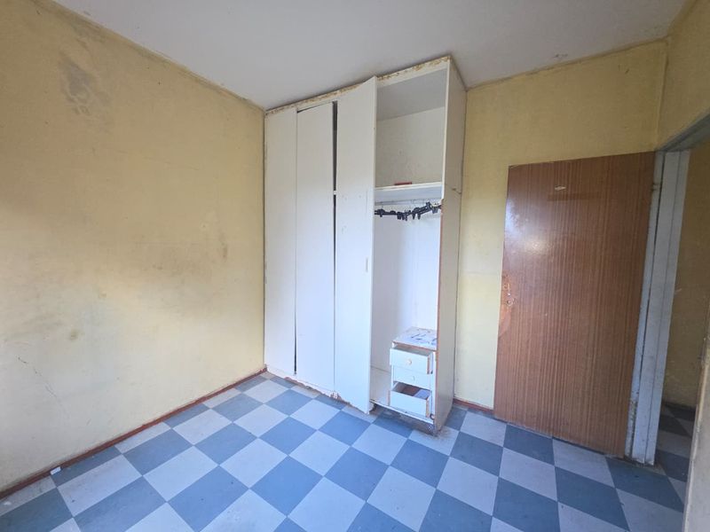 A vacant bedroom featuring built-in wardrobe storage and checkered floor tiles, requiring cosmetic updates and painting to restore its appeal.