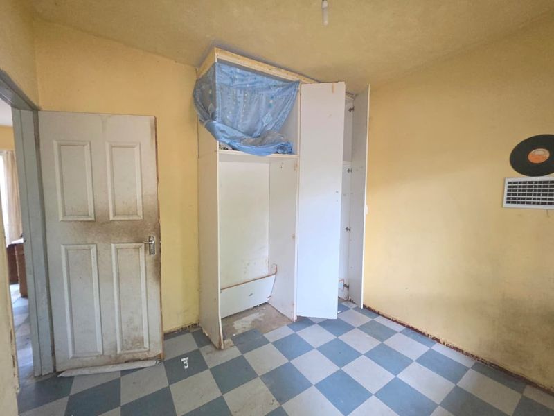A bedroom featuring built-in wardrobe storage, tiled flooring, and an air conditioning vent, currently requiring significant cosmetic refurbishment and repairs.