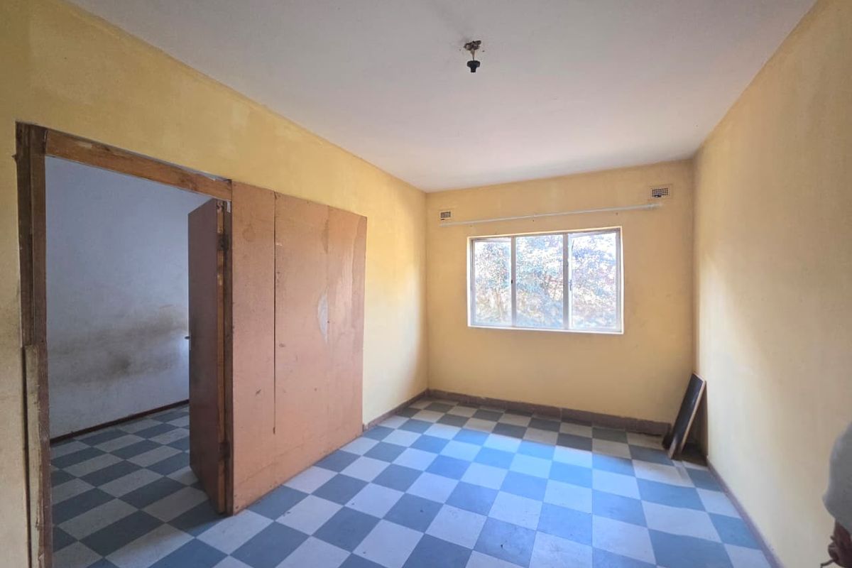 An empty bedroom featuring checkered vinyl flooring, a built-in cupboard, and a window, requiring cosmetic updates to improve its overall condition.