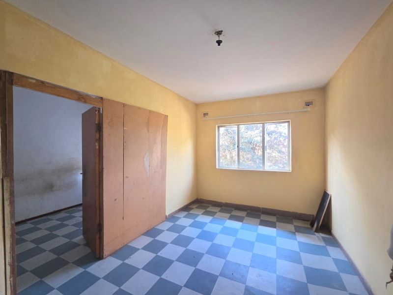 An empty bedroom featuring checkered vinyl flooring, a built-in cupboard, and a window, requiring cosmetic updates to improve its overall condition.