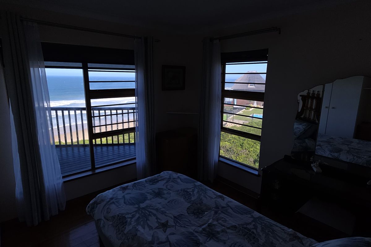 Bedroom featuring timber flooring, built-in cupboards, and louvered windows offering expansive ocean views.