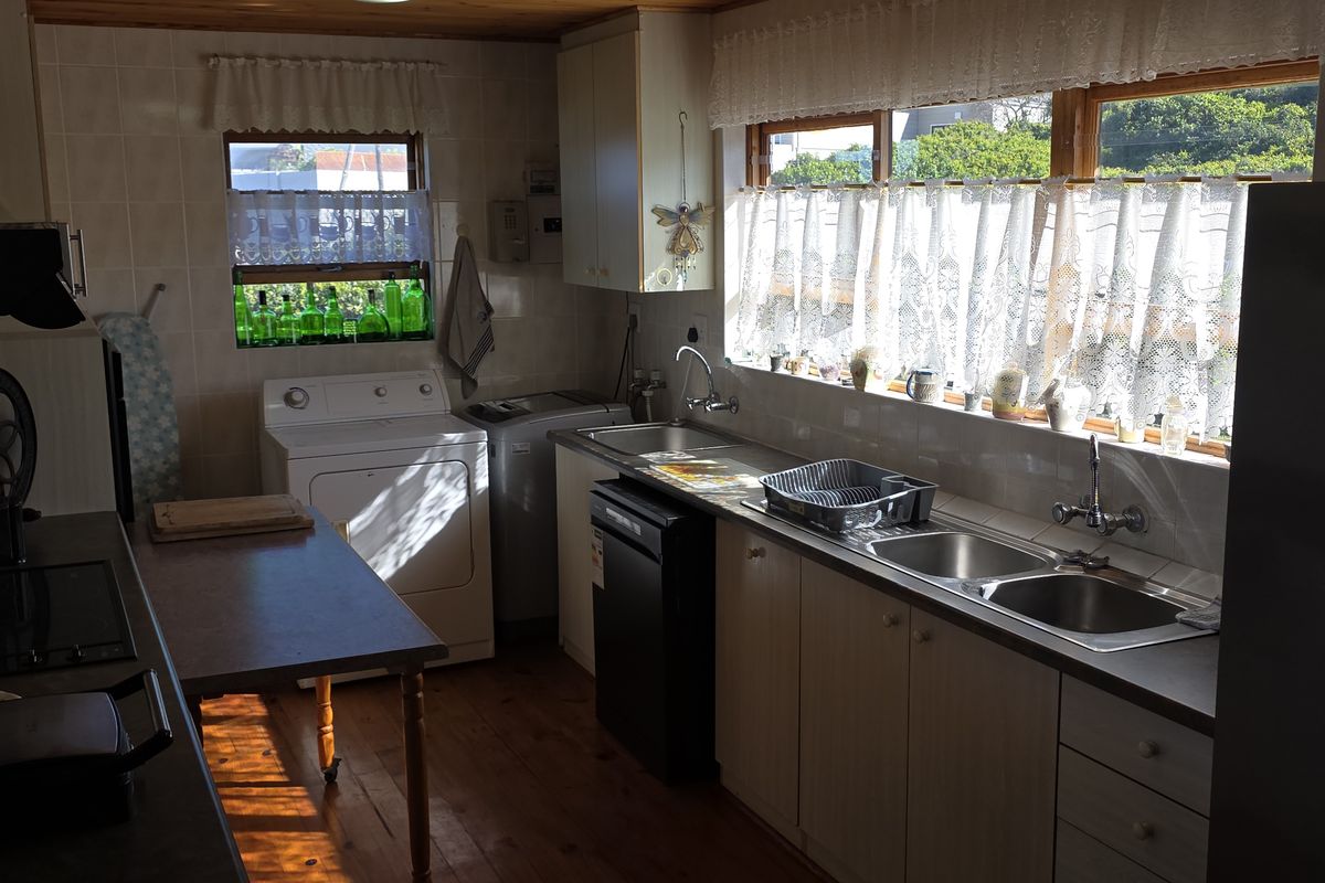 Functional kitchen featuring timber cabinetry, double stainless steel sink, tiled splashbacks, and timber flooring with natural light.