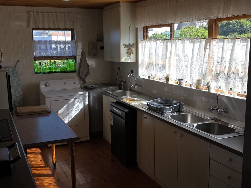 Functional kitchen featuring timber cabinetry, double stainless steel sink, tiled splashbacks, and timber flooring with natural light.