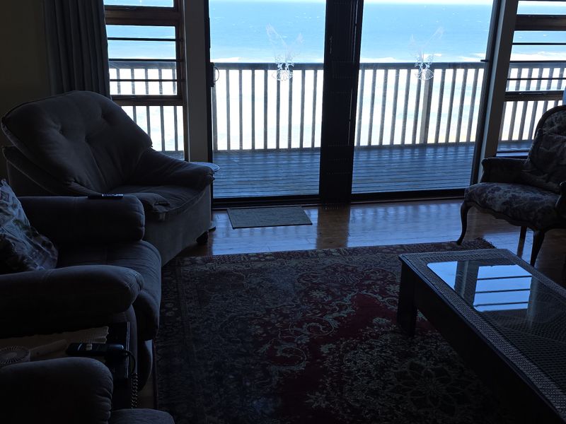 A living room featuring timber flooring and large sliding glass doors that open onto a balcony with ocean views.
