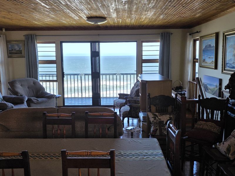 Spacious open-plan living and dining area featuring a warm timber ceiling and large sliding doors that open to a balcony with ocean views.