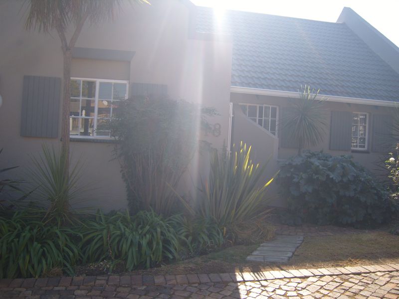 Front facade of the townhouse featuring a tiled roof, window shutters, and a paved driveway entrance with established garden landscaping.