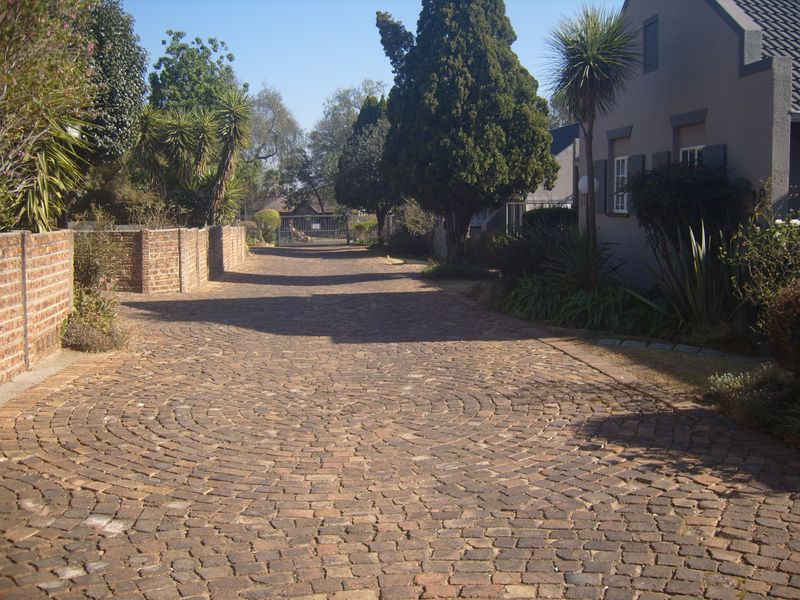 A charming cobblestone driveway leading to the front of the townhouse, featuring established landscaping and a brick boundary wall.