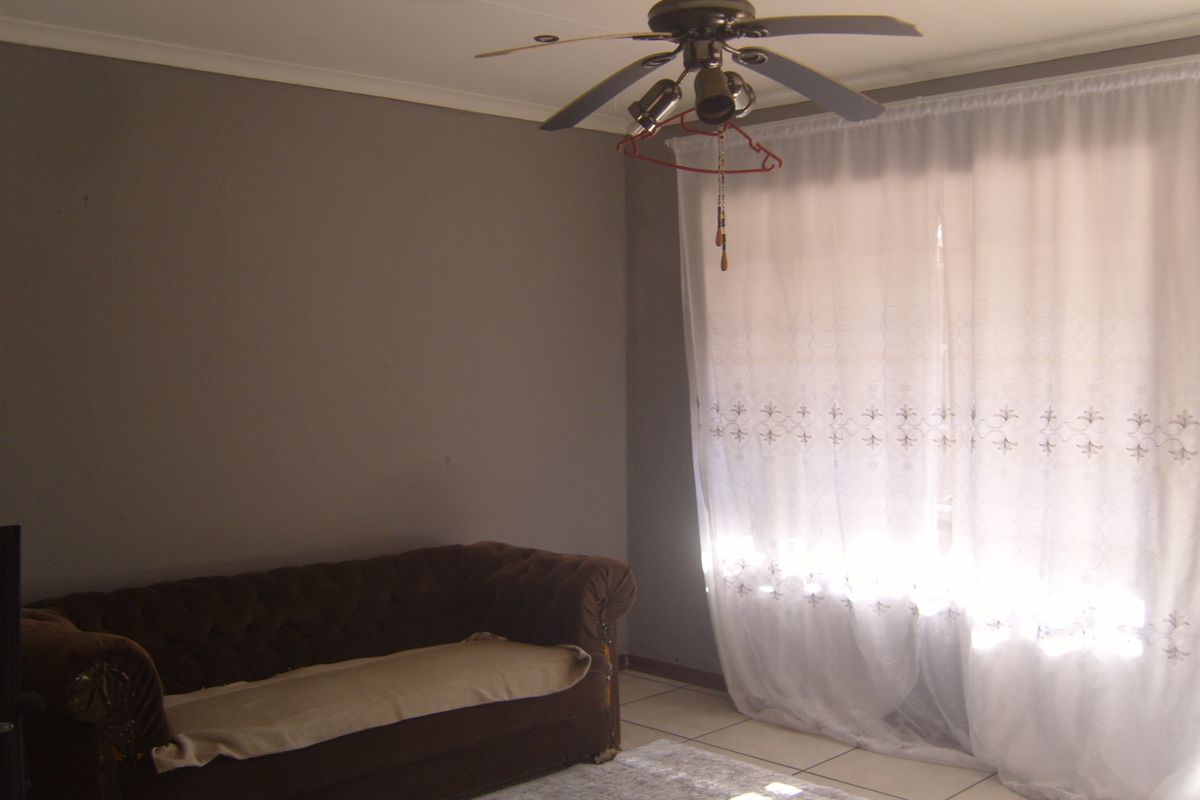 A living room featuring tiled flooring, a ceiling fan, and natural light through window coverings.