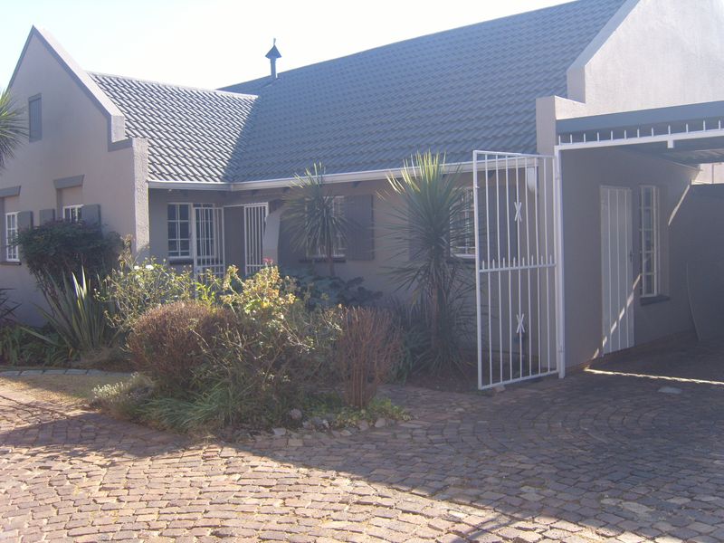Front elevation of a townhouse featuring a tiled roof, cobblestone driveway, and a covered carport area with security gate access.
