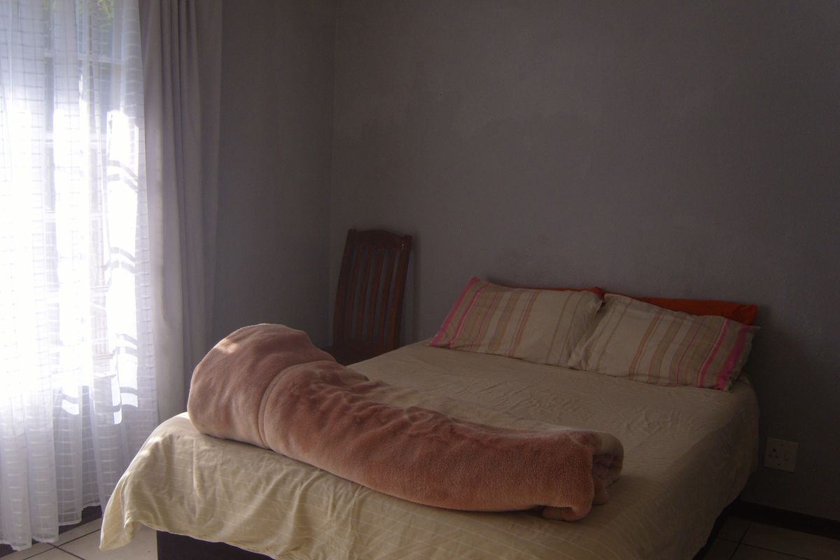 A simple bedroom featuring tiled flooring and natural light from a window with curtain rails.
