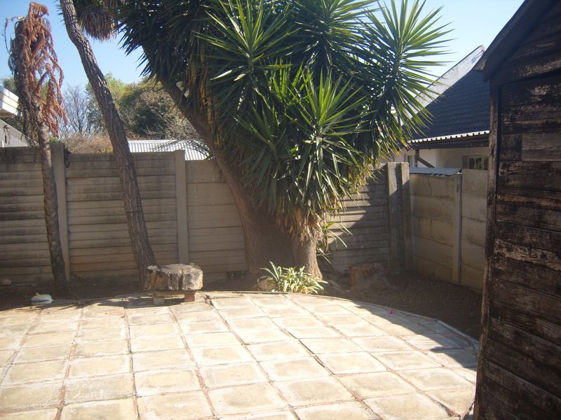A rear garden area featuring a paved patio, precast concrete boundary walls, and a weathered wooden storage shed.