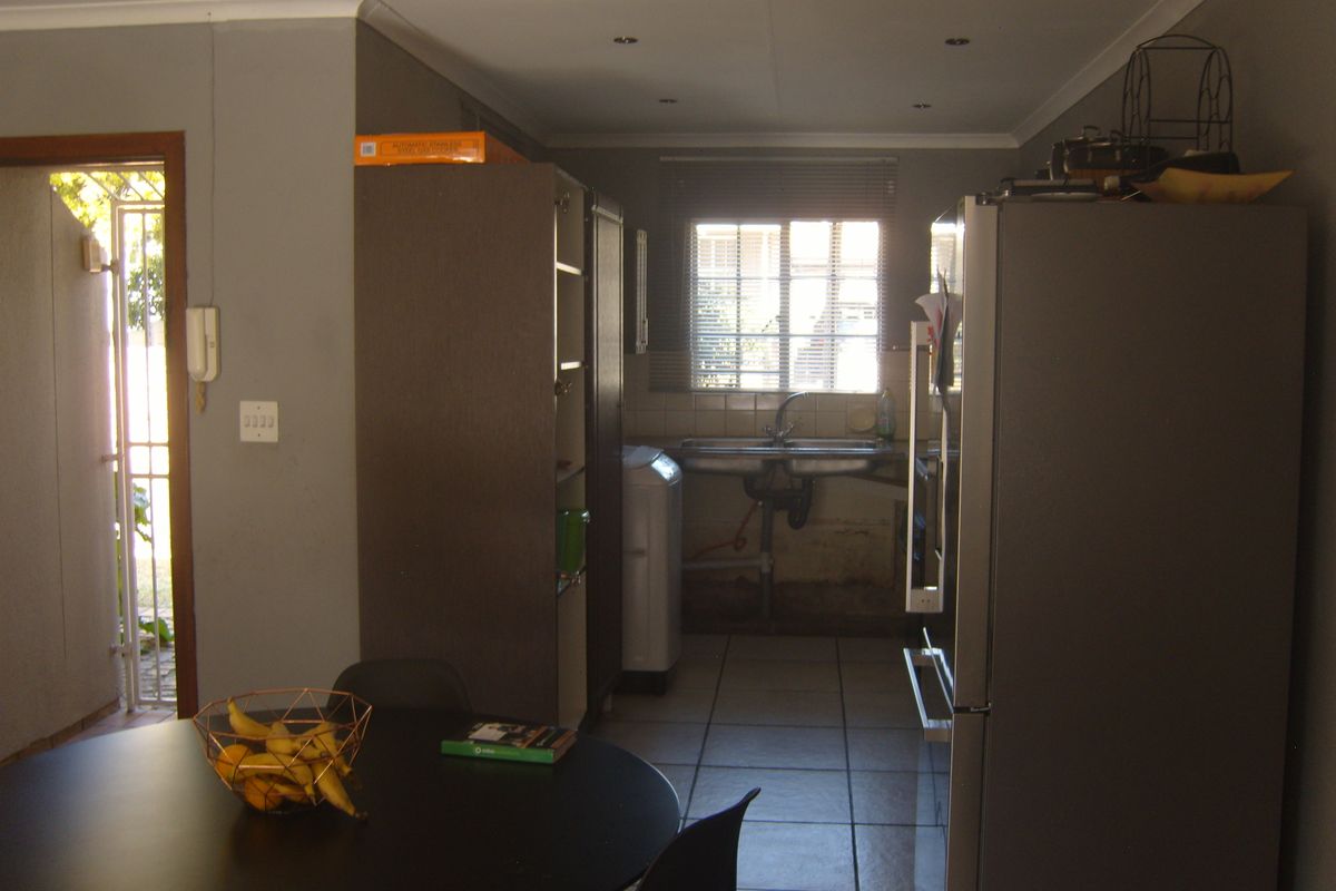 A functional kitchen area featuring tiled flooring, a double basin sink, and direct access to an exterior entrance with a security gate.