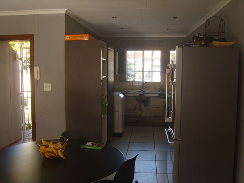 A functional kitchen area featuring tiled flooring, a double basin sink, and direct access to an exterior entrance with a security gate.