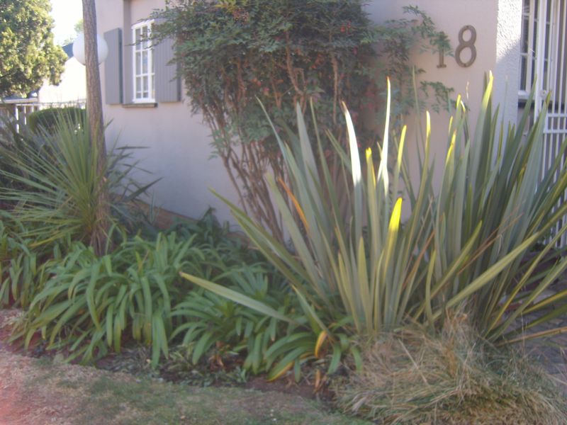 Front exterior view of the townhouse featuring established garden landscaping, security gate, and window shutters.