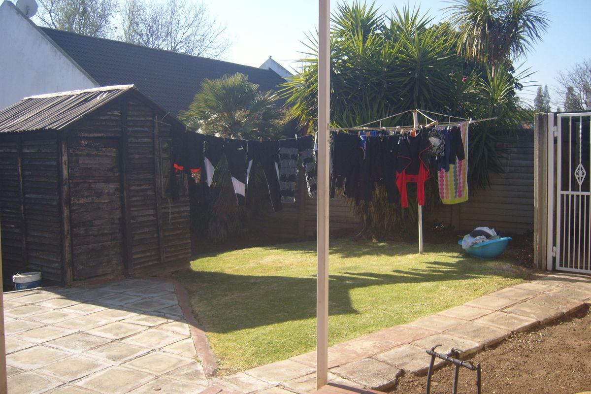 A rear garden area featuring a small lawn, paved patio space, and a wooden storage shed enclosed by boundary fencing.