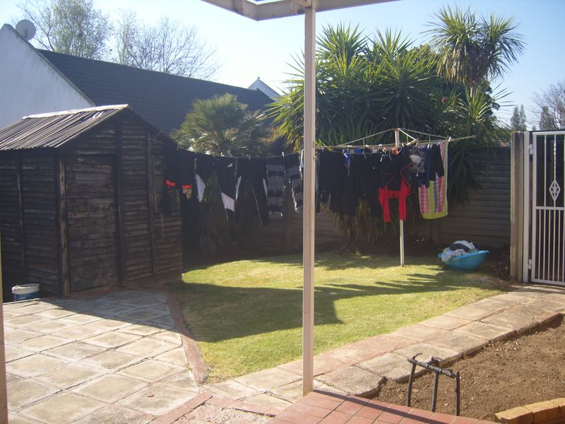 A rear garden area featuring a small lawn, paved patio space, and a wooden storage shed enclosed by boundary fencing.