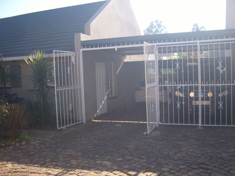 A covered carport area with a secure metal gate and paved driveway access.