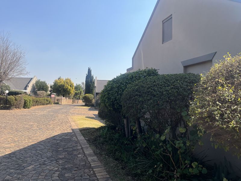 A view of the townhouse complex street featuring a cobblestone driveway and well-maintained garden landscaping along the exterior wall.