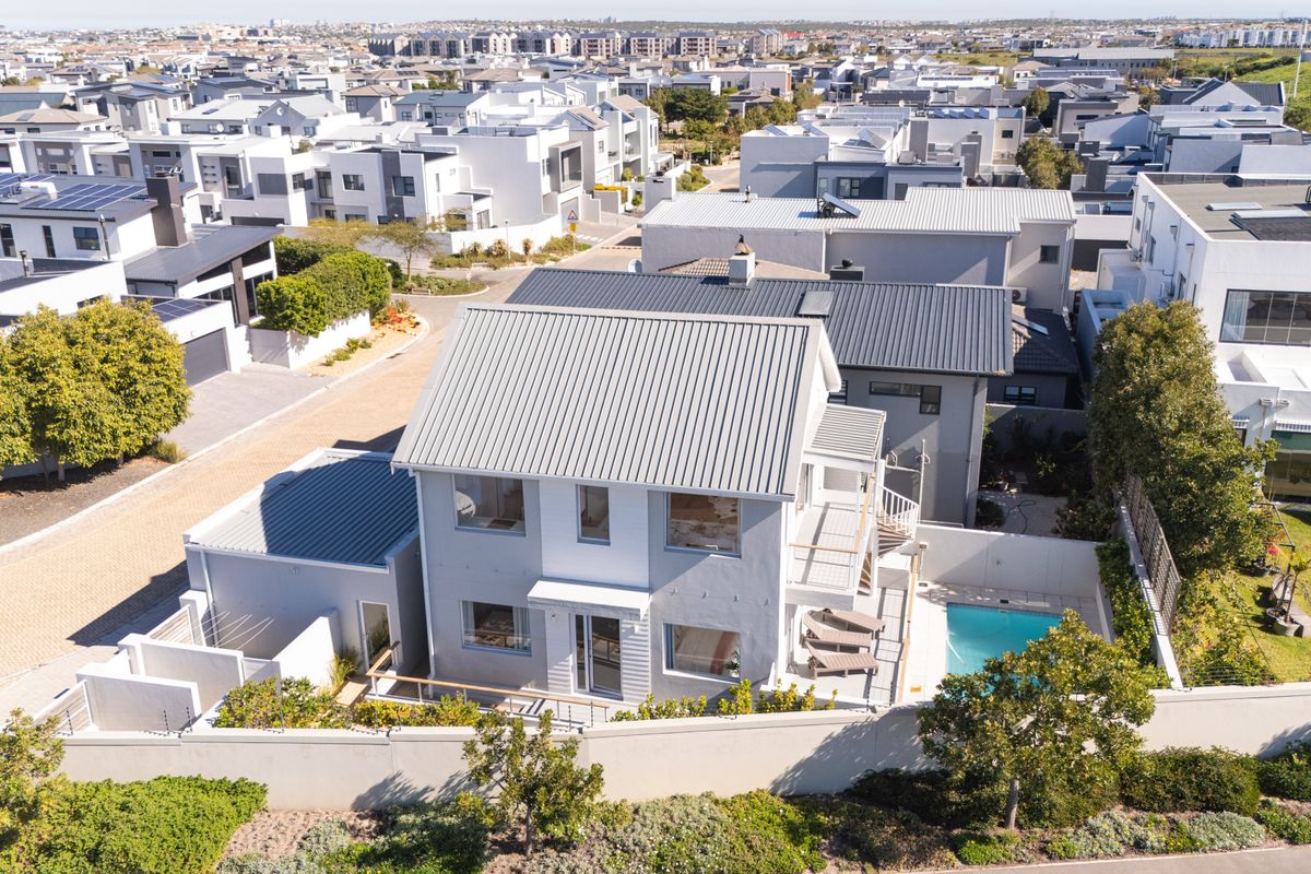 Aerial view of a modern two-story residential property featuring a metal roof, private swimming pool, and balcony within a well-maintained estate.