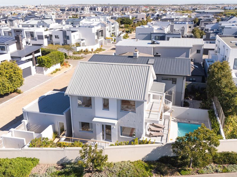 Aerial view of a modern two-story residential property featuring a metal roof, private swimming pool, and balcony within a well-maintained estate.