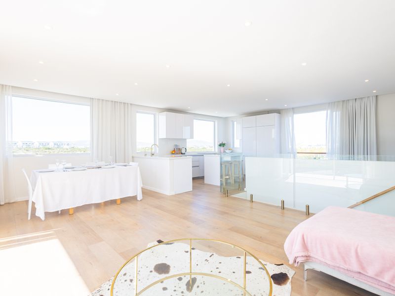 Bright and spacious open-plan living area featuring modern kitchen cabinetry, light timber flooring, and a glass balustrade overlooking the lower level.