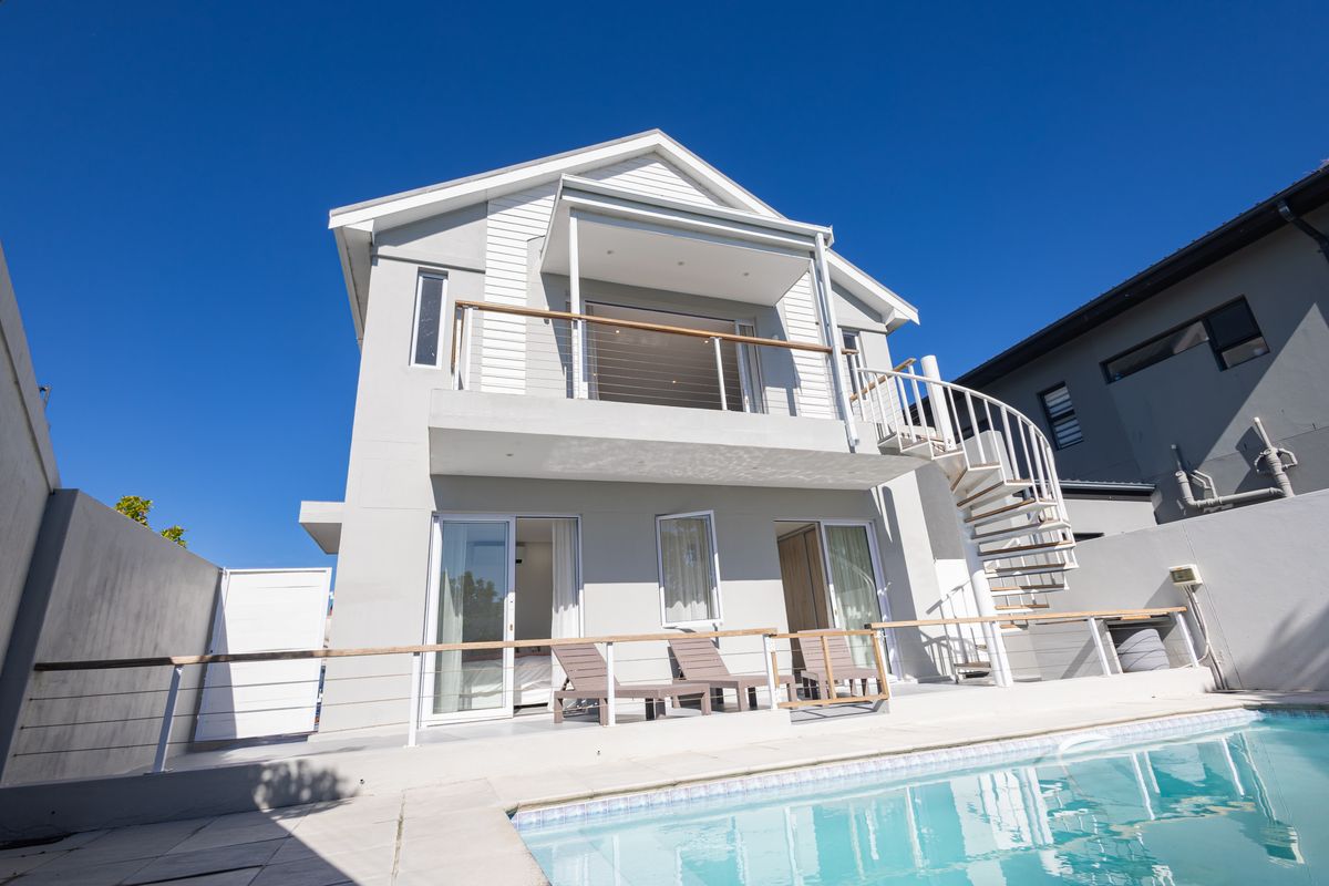 Rear view of a modern two-story house featuring a swimming pool, paved deck, balcony, and an external spiral staircase.