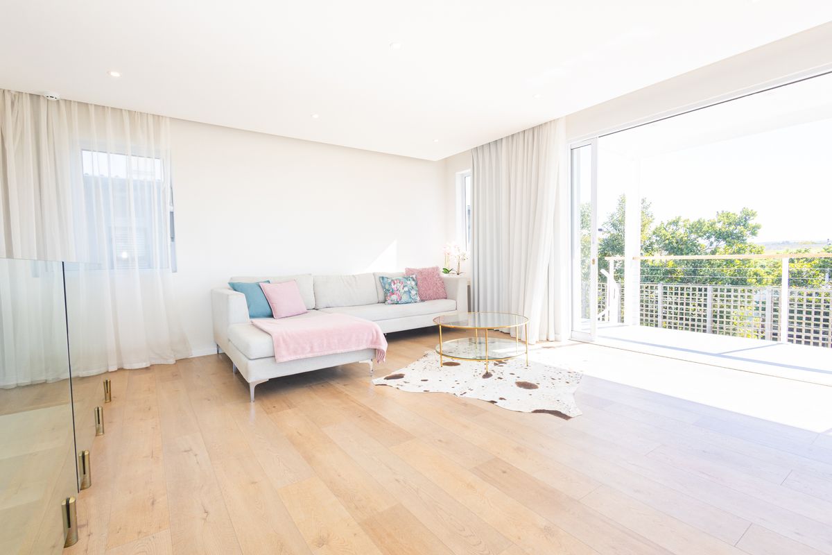 Bright and modern living room featuring light hardwood flooring, recessed lighting, and large sliding glass doors opening onto an outdoor balcony.