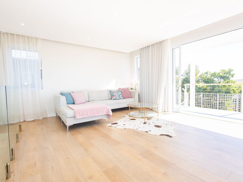 Bright and modern living room featuring light hardwood flooring, recessed lighting, and large sliding glass doors opening onto an outdoor balcony.