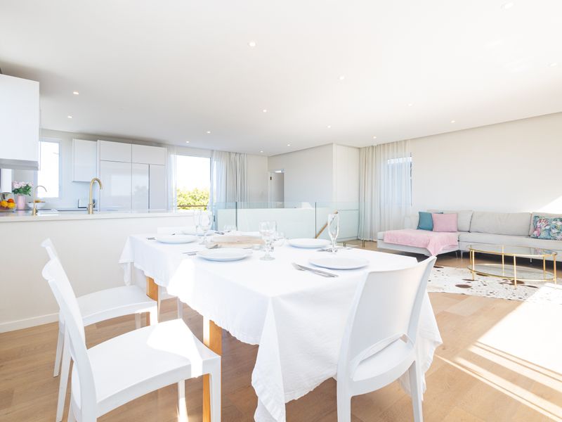 Bright and modern open-plan living, dining, and kitchen area featuring hardwood flooring, recessed lighting, and a sleek glass balustrade.