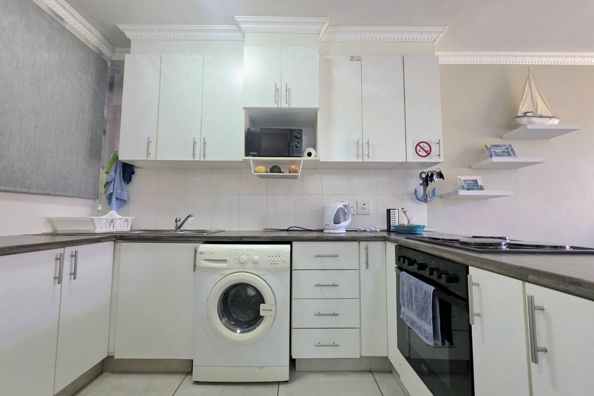 A functional kitchen featuring white cabinetry, laminate countertops, built-in oven, hob, and integrated laundry appliance space, finished with decorative crown molding.