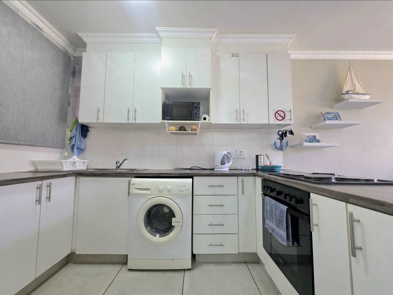 A functional kitchen featuring white cabinetry, laminate countertops, built-in oven, hob, and integrated laundry appliance space, finished with decorative crown molding.