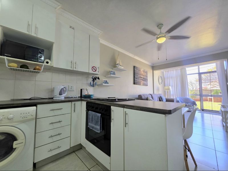 Open-plan kitchen and living area featuring white cabinetry, dark countertops, built-in oven, tiled floors, and direct access to an outdoor patio area.