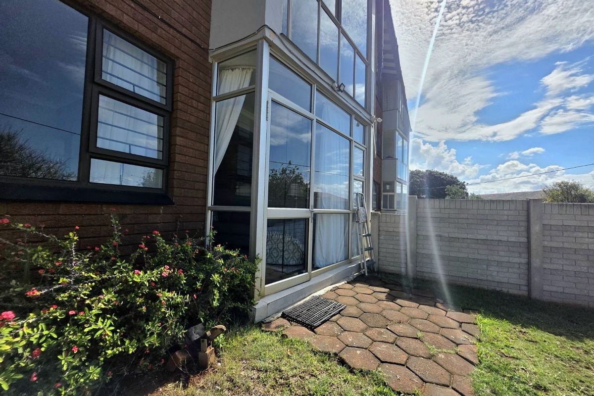 Rear exterior view of the apartment featuring a brick facade, large aluminium-framed windows, and a paved patio area leading to a small garden.