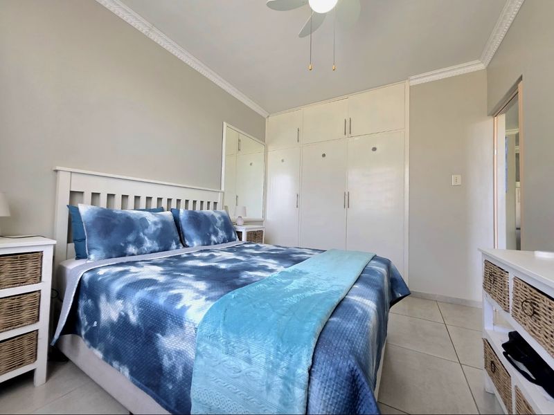 A well-maintained bedroom featuring built-in cupboards, tiled flooring, and a ceiling fan, offering a clean and functional living space.