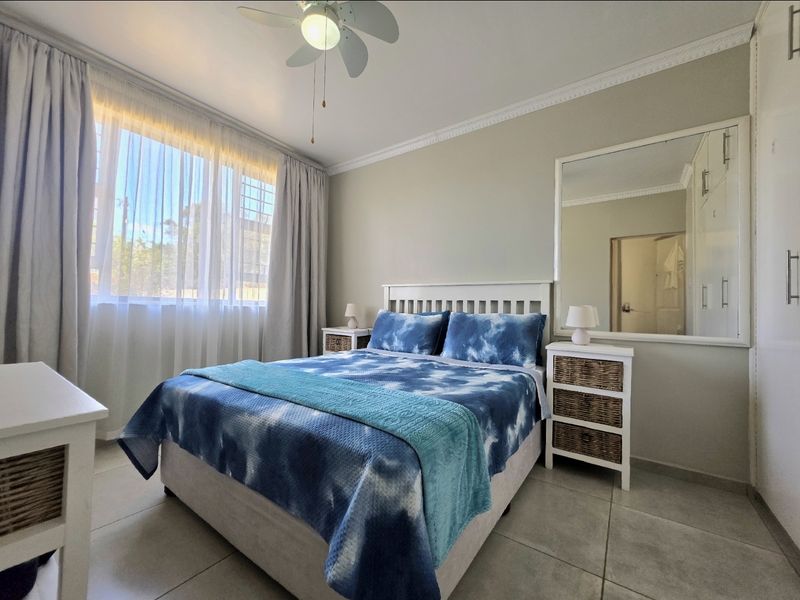 A well-maintained bedroom featuring tiled flooring, built-in cupboards, a ceiling fan, and decorative cornice detailing.