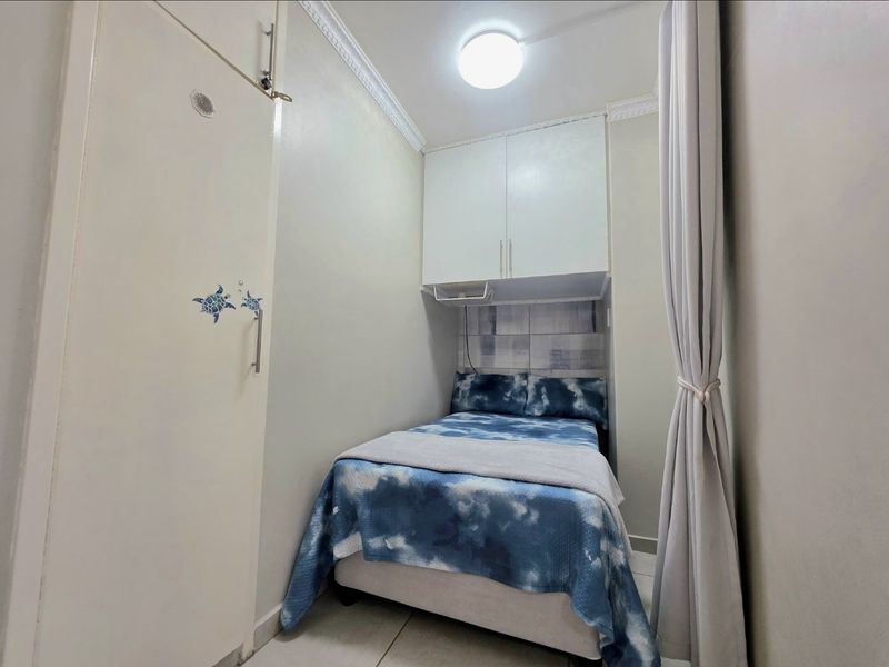 A compact bedroom featuring built-in overhead cabinetry, decorative ceiling cornicing, and tiled flooring.